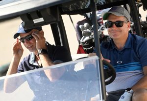 An image of two men in a golf cart, both smiling.
